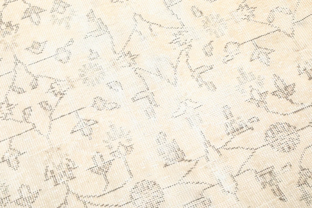 Close-up detail of the hand-knotted wool pile and faded gray patterns on the ivory field