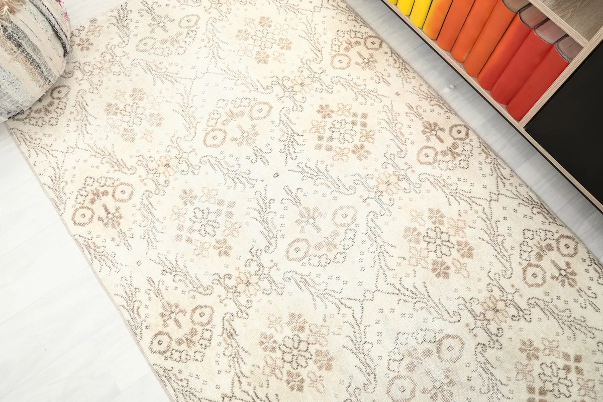 Angled view of the ivory and tan rug's surface, showing the subtle variations in its vintage wool pile.