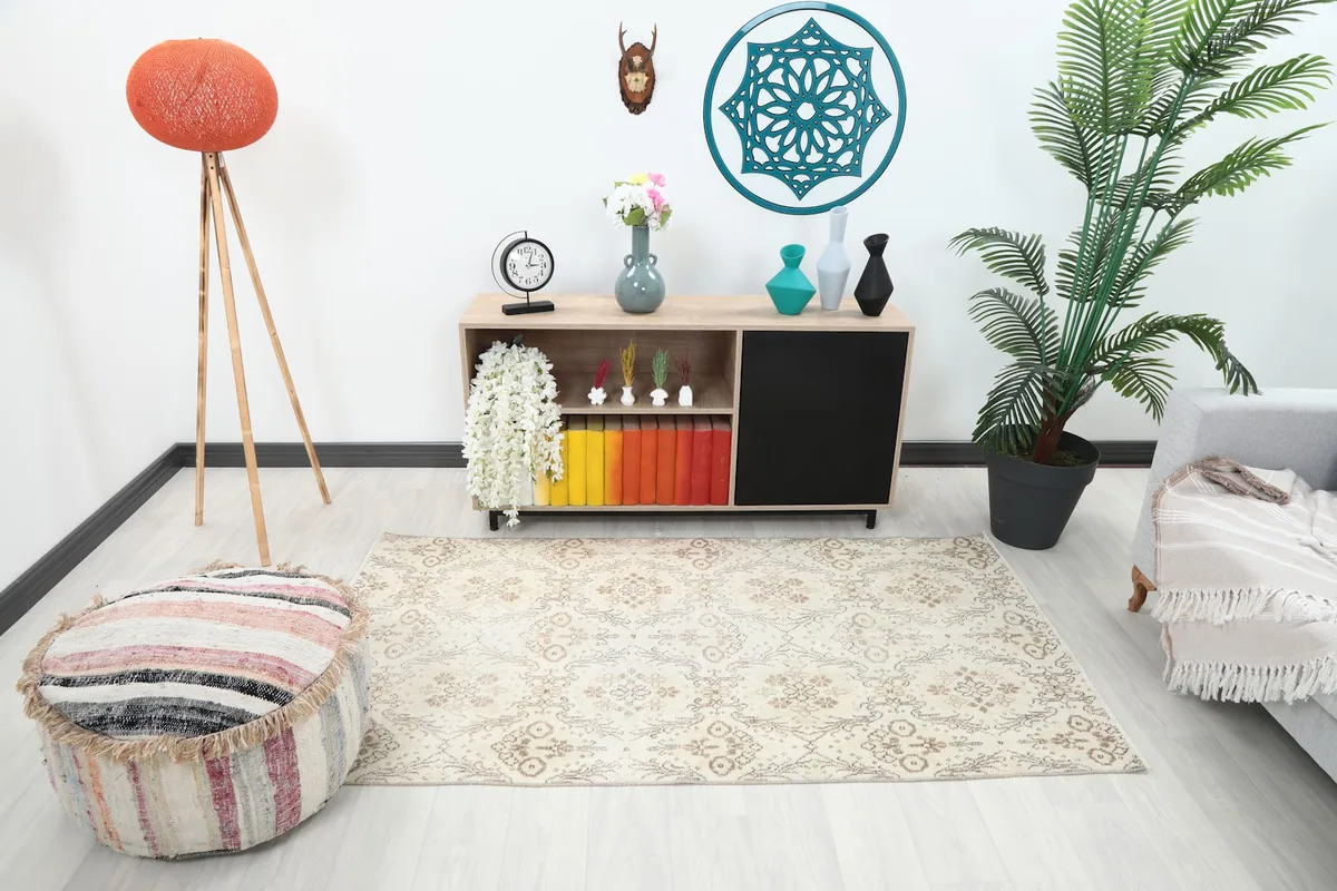 Ivory and tan vintage rug placed in a modern living room setting with a light sofa and wooden furniture.