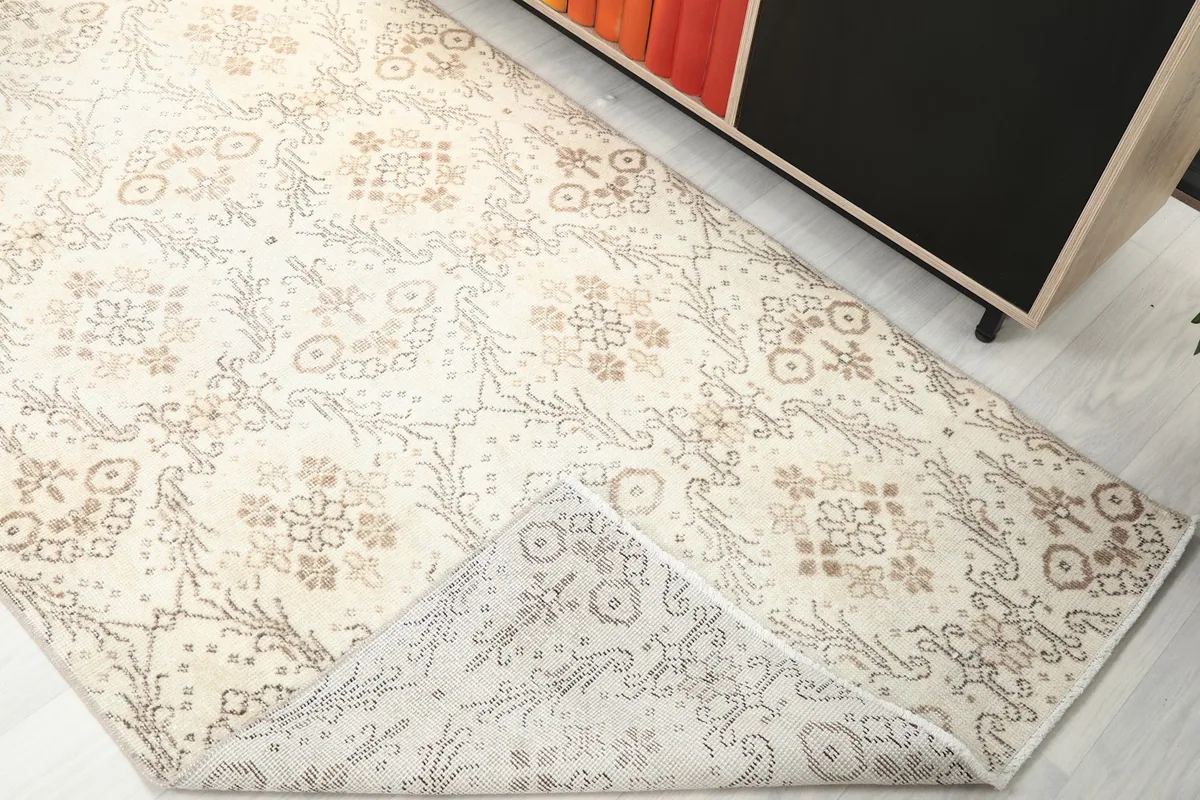 Corner of the ivory and tan rug folded back to reveal the cotton foundation and reverse side of the pattern.