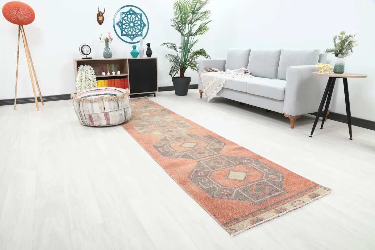 Angled view of the rust runner rug in a room, showing its length and placement near a gray sofa and pouf.