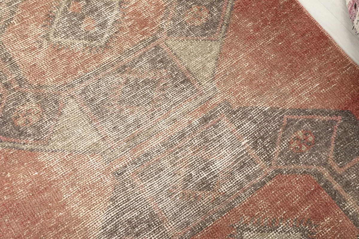 Close-up detail of the rug's low wool pile, showing the texture and faded appearance of the rust and gray colors.