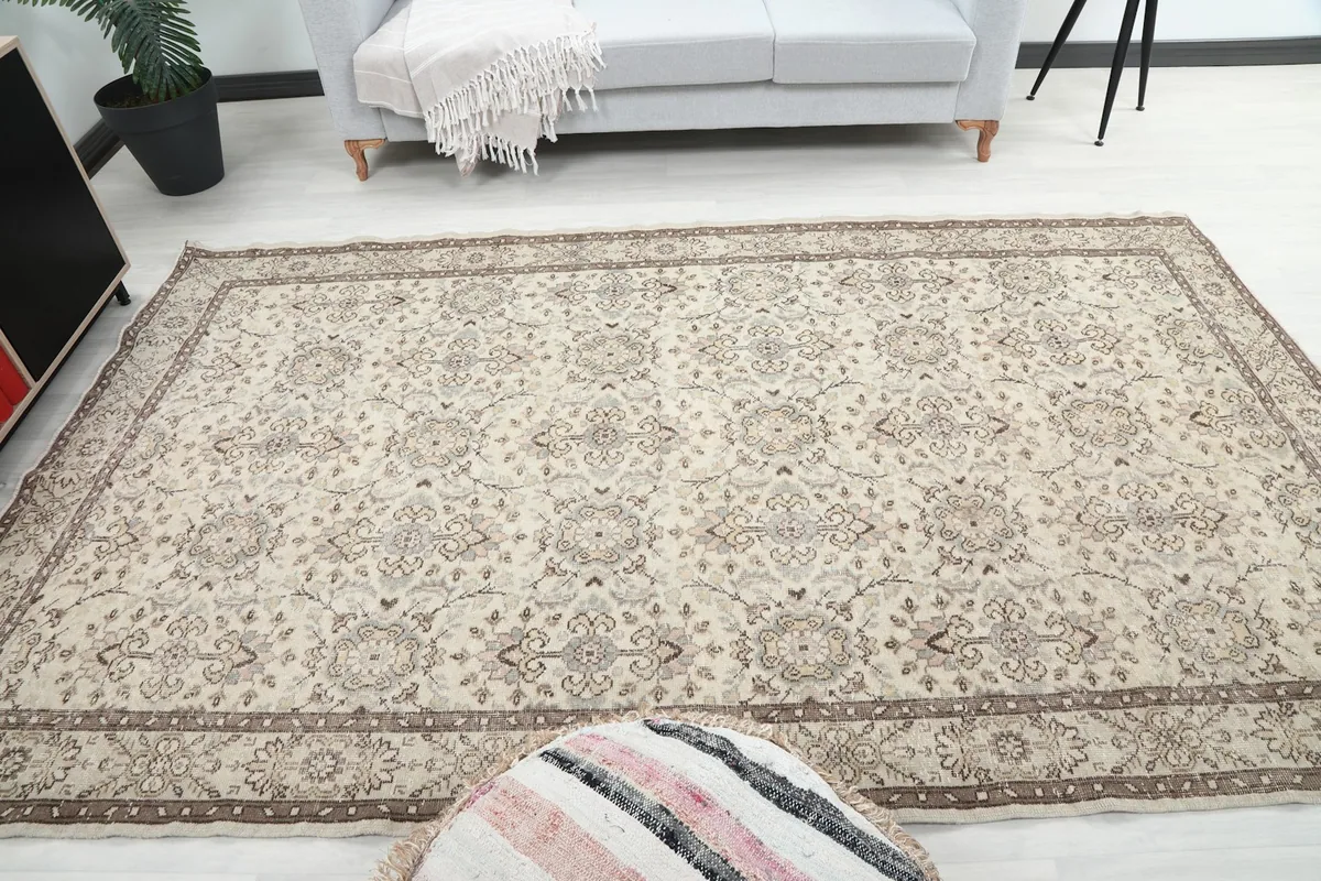 Rug placed in a room, with a gray sofa in the background and a decorative pouf in the foreground.
