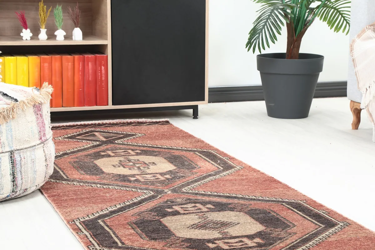 Close-up view of one end of the rust runner rug in a room, showing the geometric patterns and a pouf.