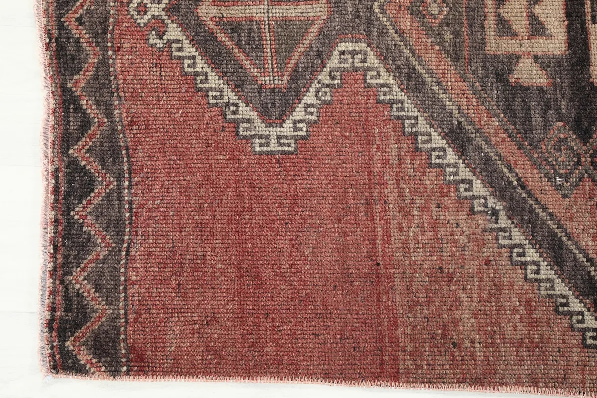 Close-up of the end of the rug, showing the fringe and the edge of the rust field with a tribal border.
