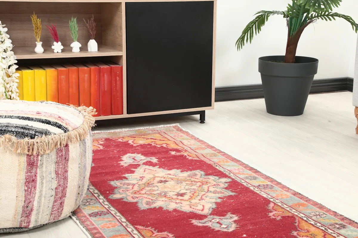 Close-up room view of the red rug's pattern and texture, next to a decorative pouf
