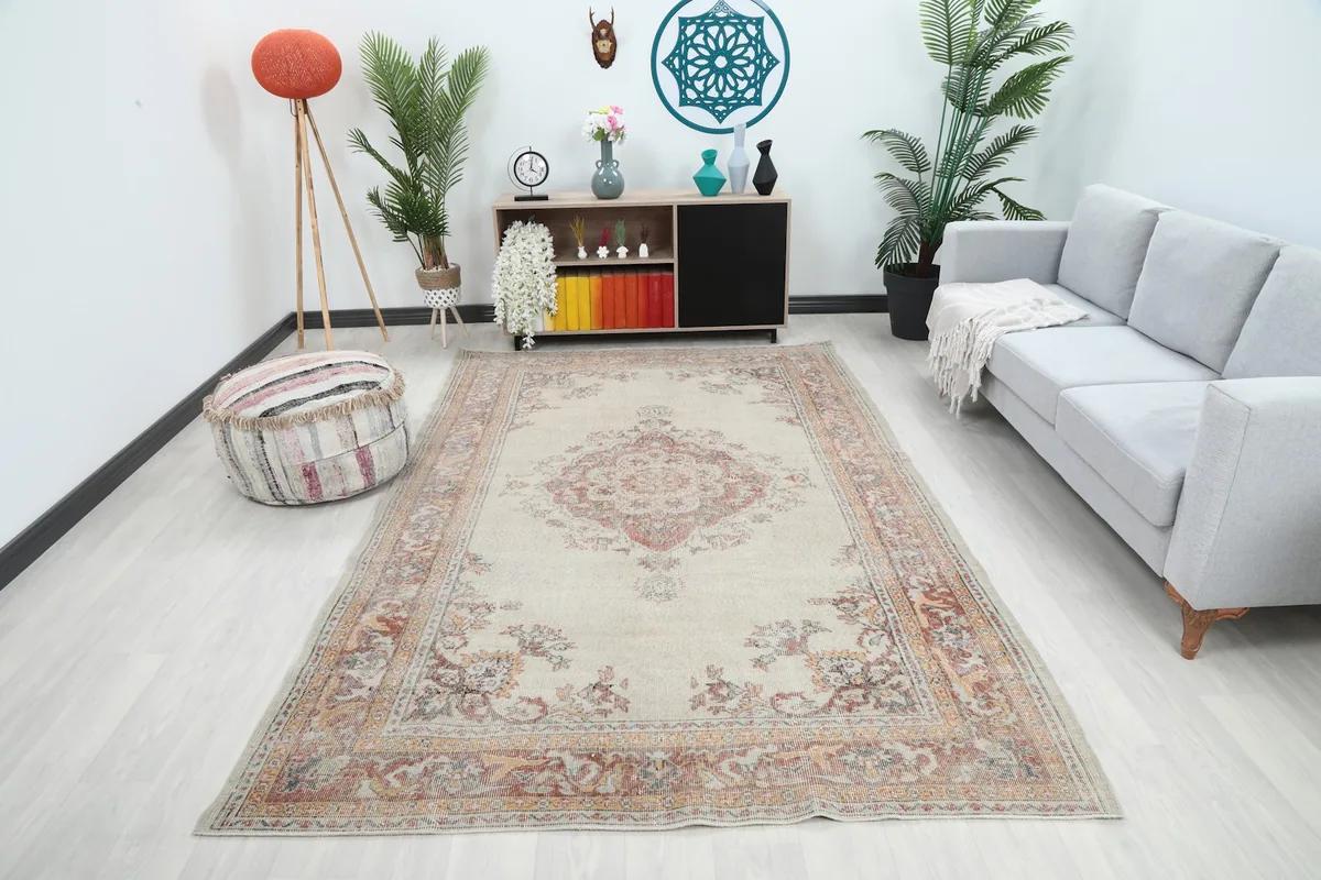 Ivory and rust vintage rug shown in a living room setting with a sofa and plants
