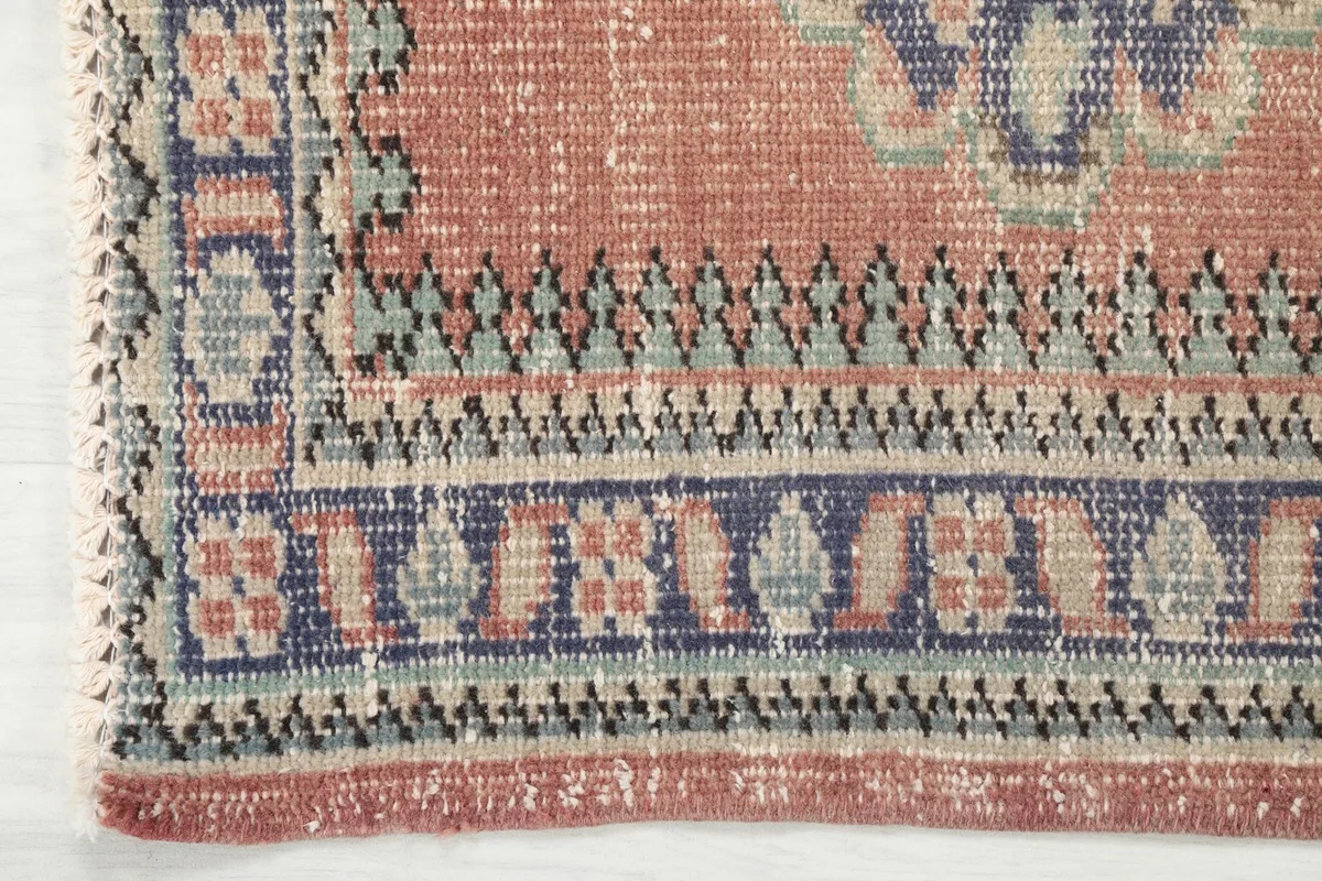 Close-up of the rug's border, revealing geometric patterns in blue, beige, and green with a rust edge