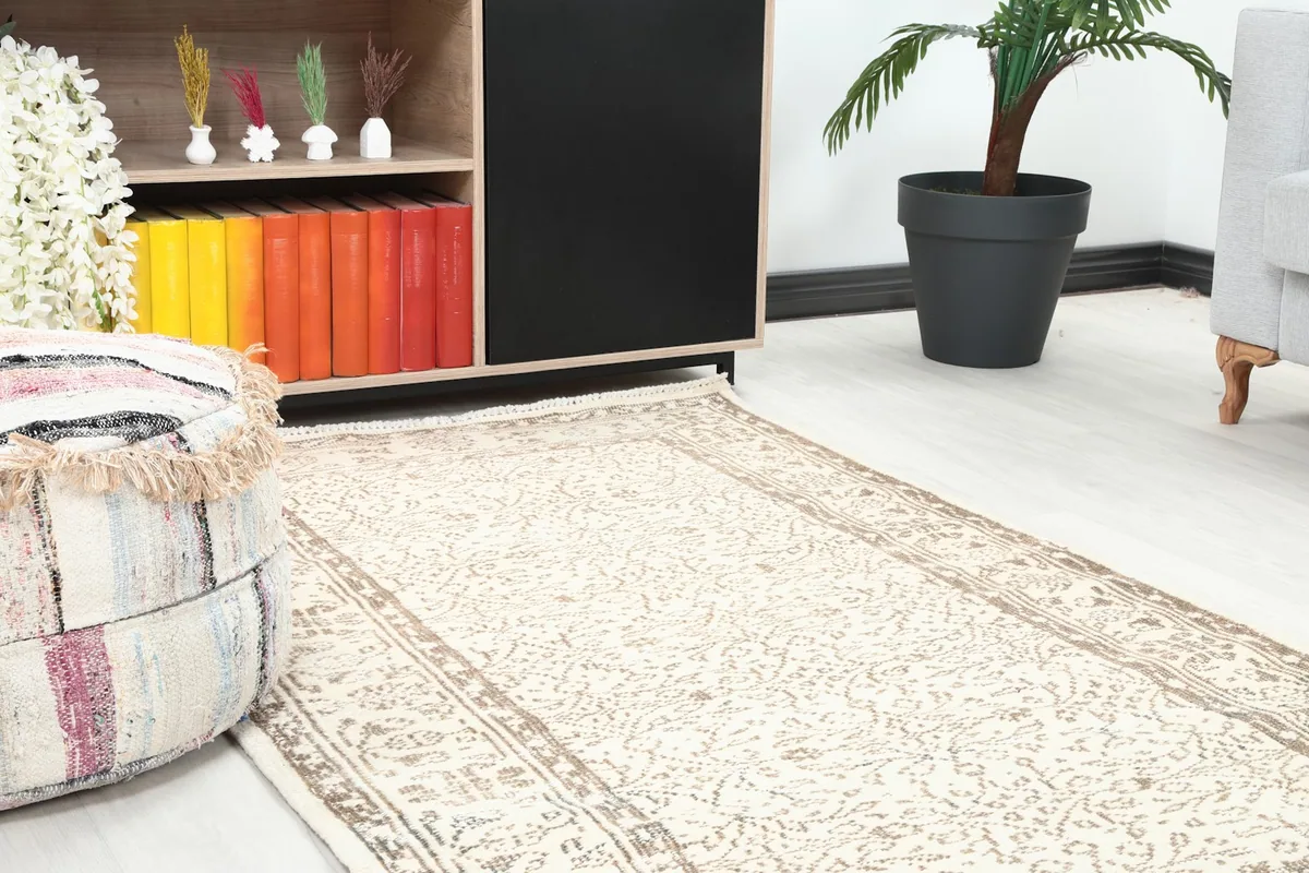 Close-up view of the vintage rug in a room, showing its placement near a pouf and cabinet