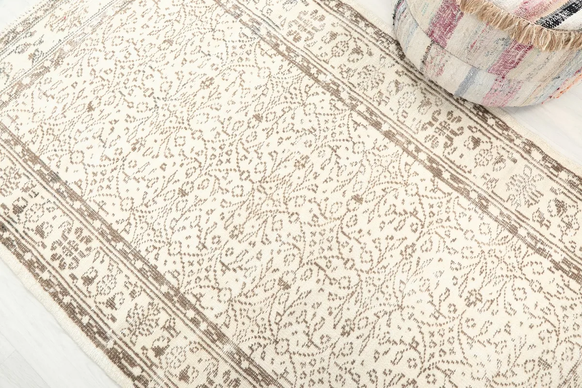 Close-up detail of the ivory field and tan floral and geometric patterns of the rug