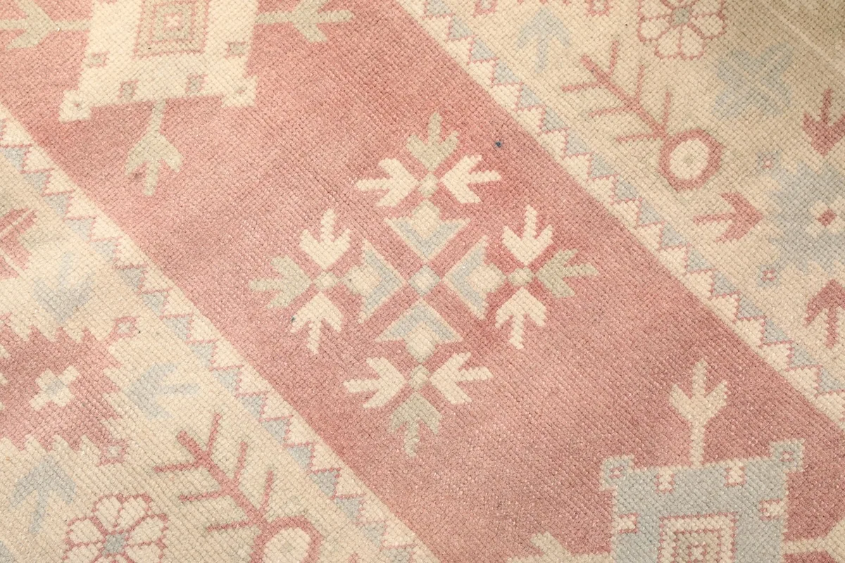 Close-up detail of the hand-knotted geometric patterns and color variations in rose and blue.