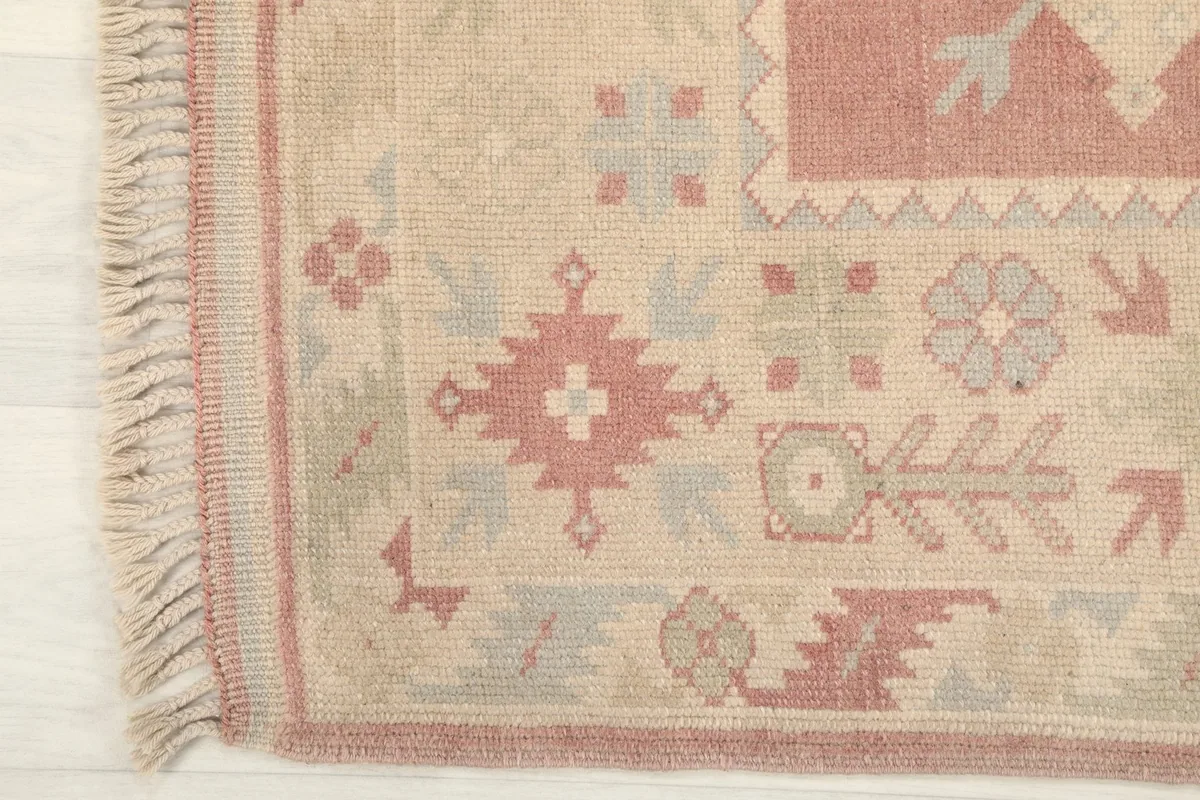 Detail of the rug's edge and fringe, showing the beige field and rose accents.