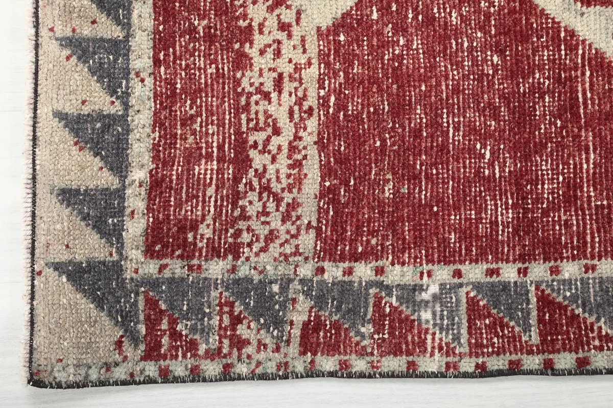 Close-up of the rug's edge, revealing the distressed red pile and the gray and beige border pattern.