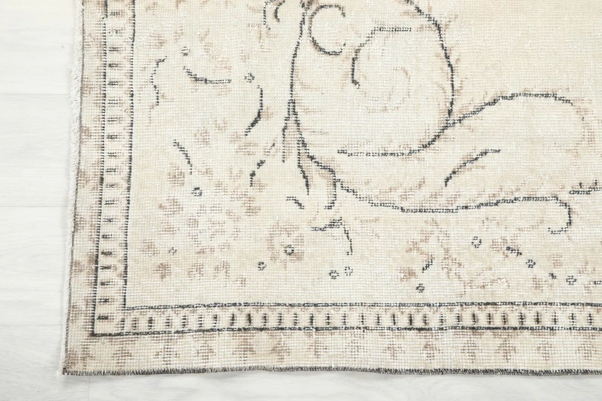 Close-up of the rug's border, showing the faded gray and beige patterns and edge condition.