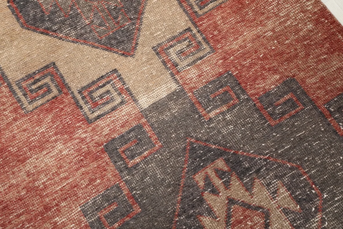 Close-up of the hand-knotted wool pile, revealing the geometric motifs and natural wear on the rust and tan areas.