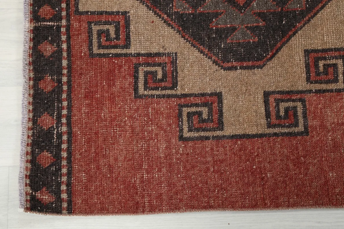 Detail of the runner's end border, showcasing the dark charcoal and black patterned edge and the rust field.