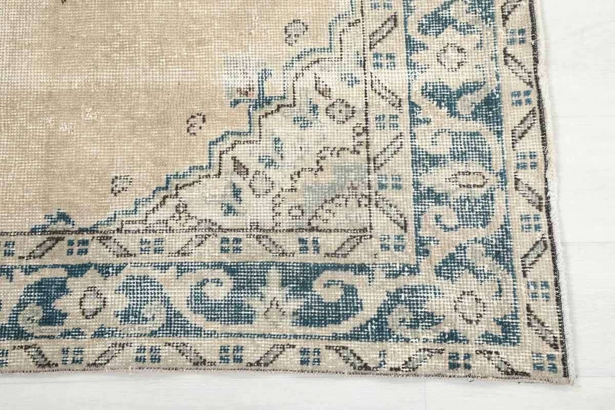Detail of the blue geometric border and corner design on the vintage tan rug.