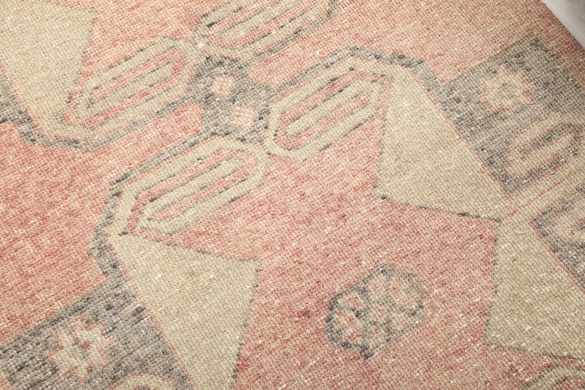 Close-up of the hand-knotted wool pile, revealing the rose, beige, and charcoal geometric patterns and texture.