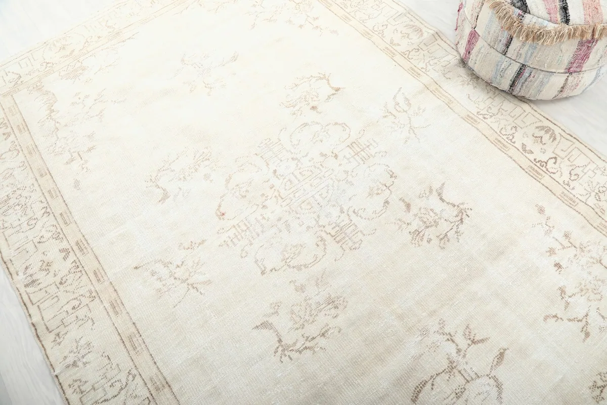 Angle view highlighting the faded central medallion and floral motifs of the cream rug