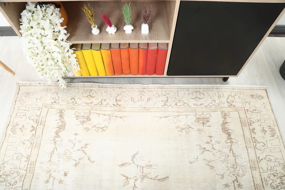 Overhead detail of the cream rug's design and border, with a glimpse of a wooden shelf