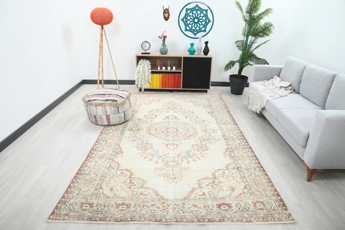 Large ivory and rust vintage rug shown in a modern living room setting with a sofa and decor