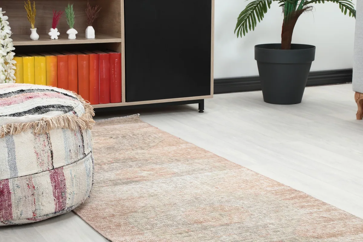 Close-up of the runner rug's end in a room setting, next to a decorative pouf and wooden cabinet