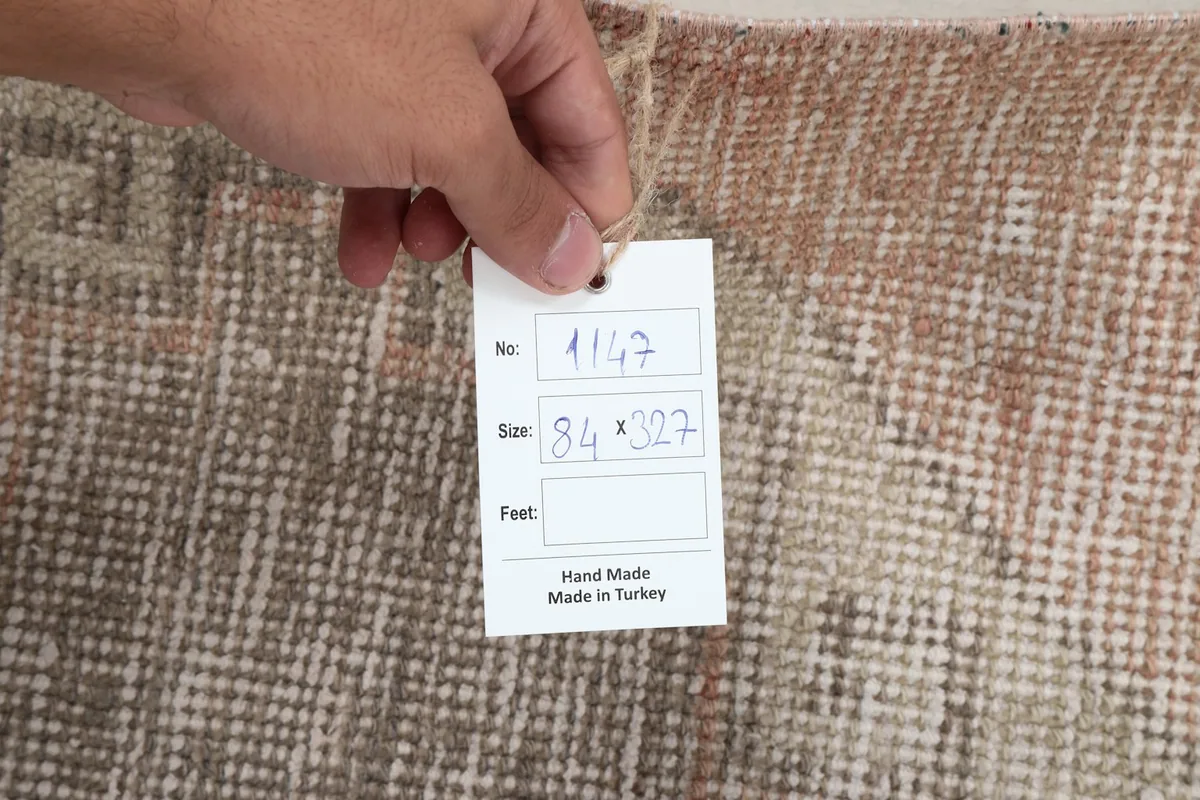 Hand holding a tag showing the rug's inventory number and dimensions (84 x 327 cm)