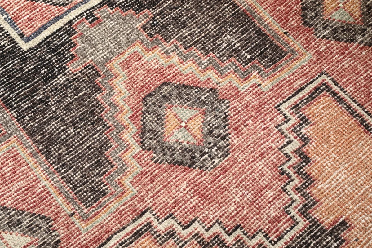 Close-up detail of the hand-knotted pile and intricate geometric pattern in rust, black, and beige