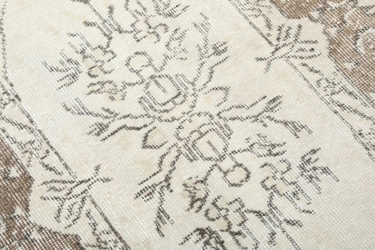 Detailed view of the hand-knotted floral patterns and muted beige and gray colors on the ivory field