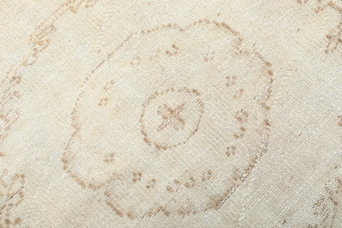 Detailed view of the intricate beige patterns within the medallion on the ivory vintage rug.