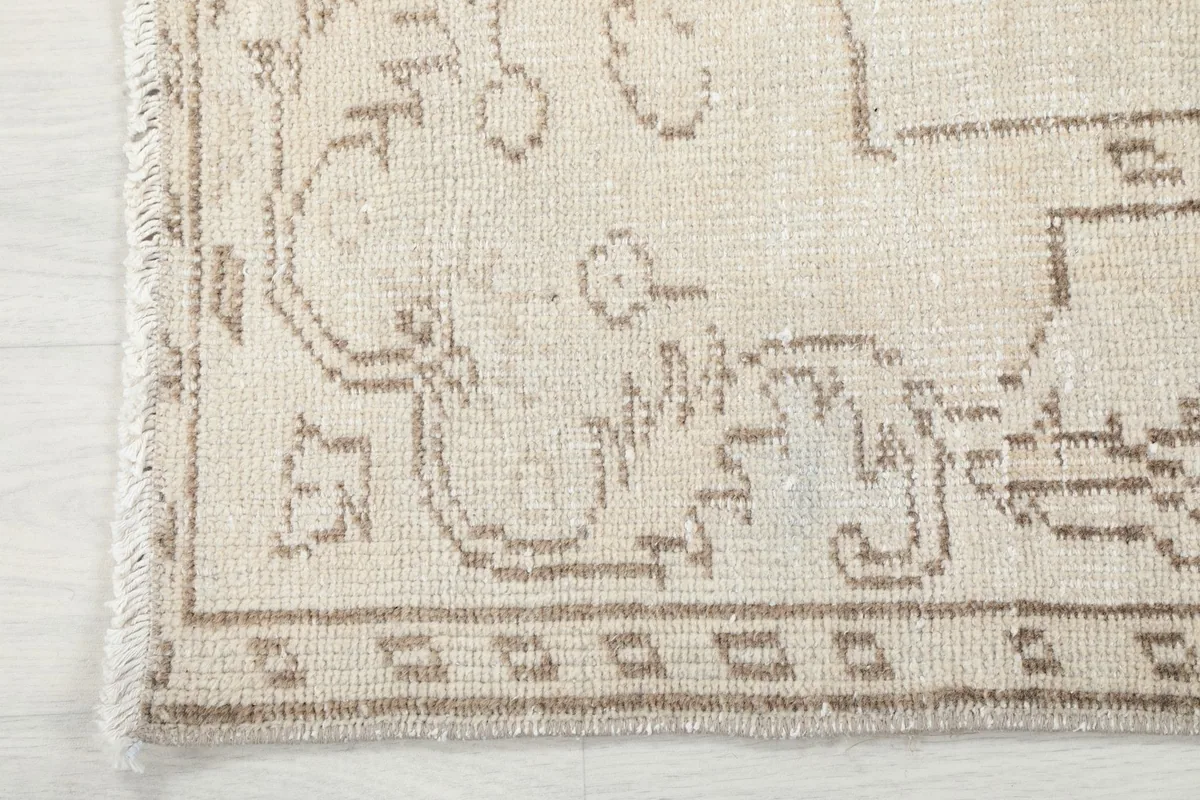 Close-up of the geometric border design and fringe on the vintage ivory and beige wool rug.