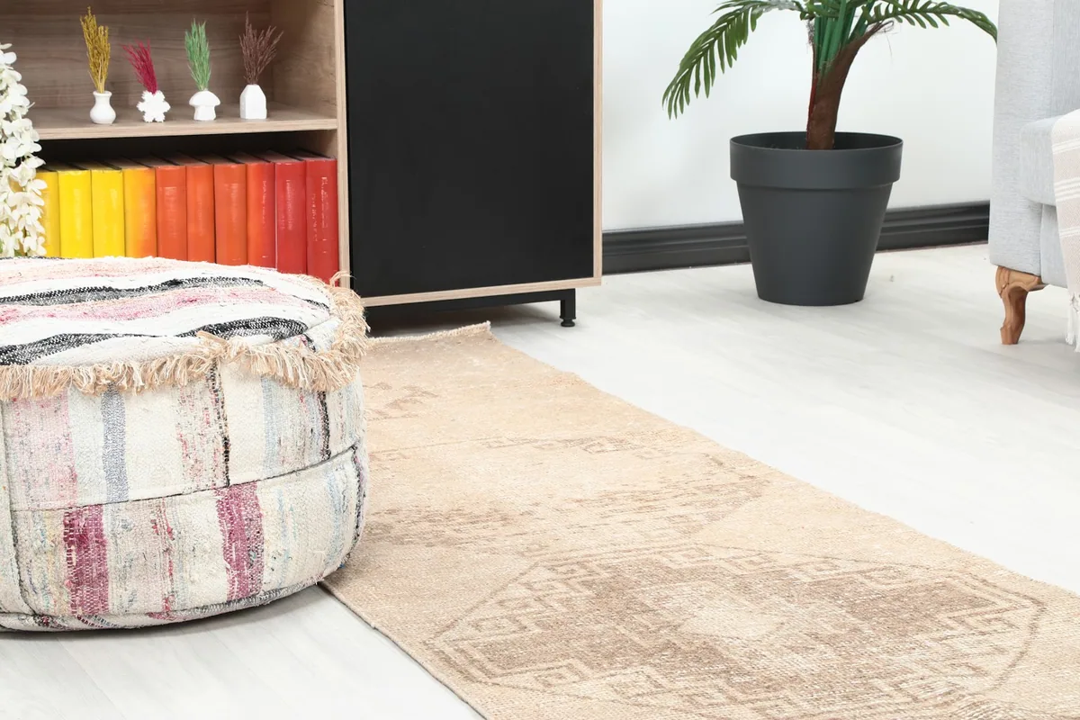 Close-up angle showing the tan field and brown geometric motifs of the runner rug next to a decorative pouf.