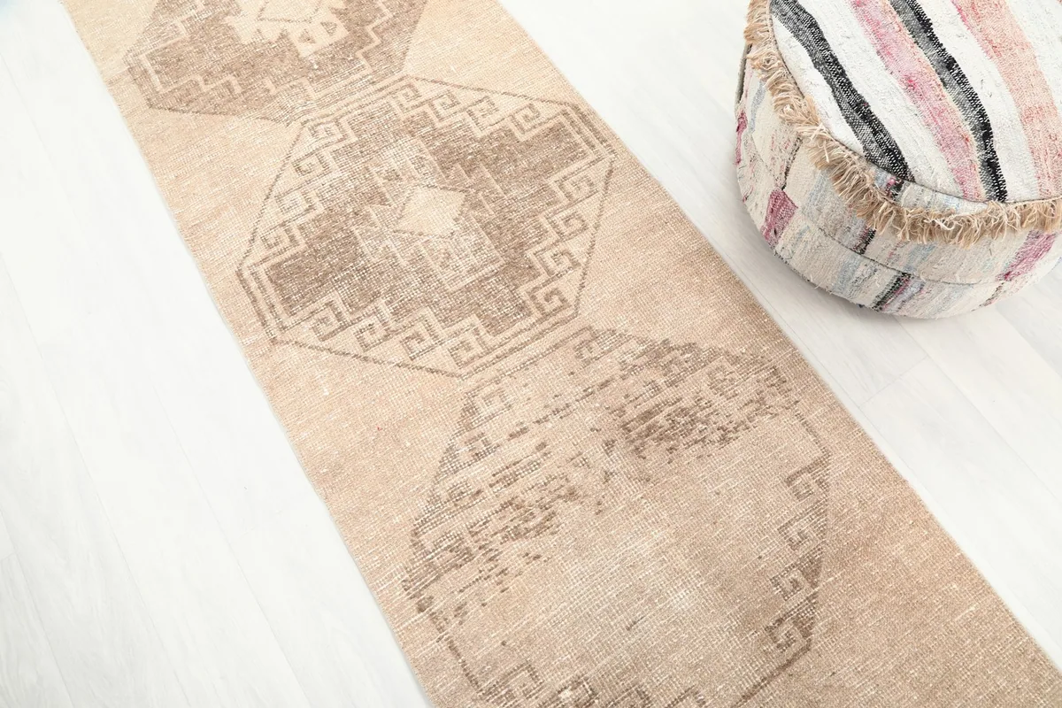 Angled view of the vintage tan runner rug, focusing on the repeating brown geometric diamond patterns.