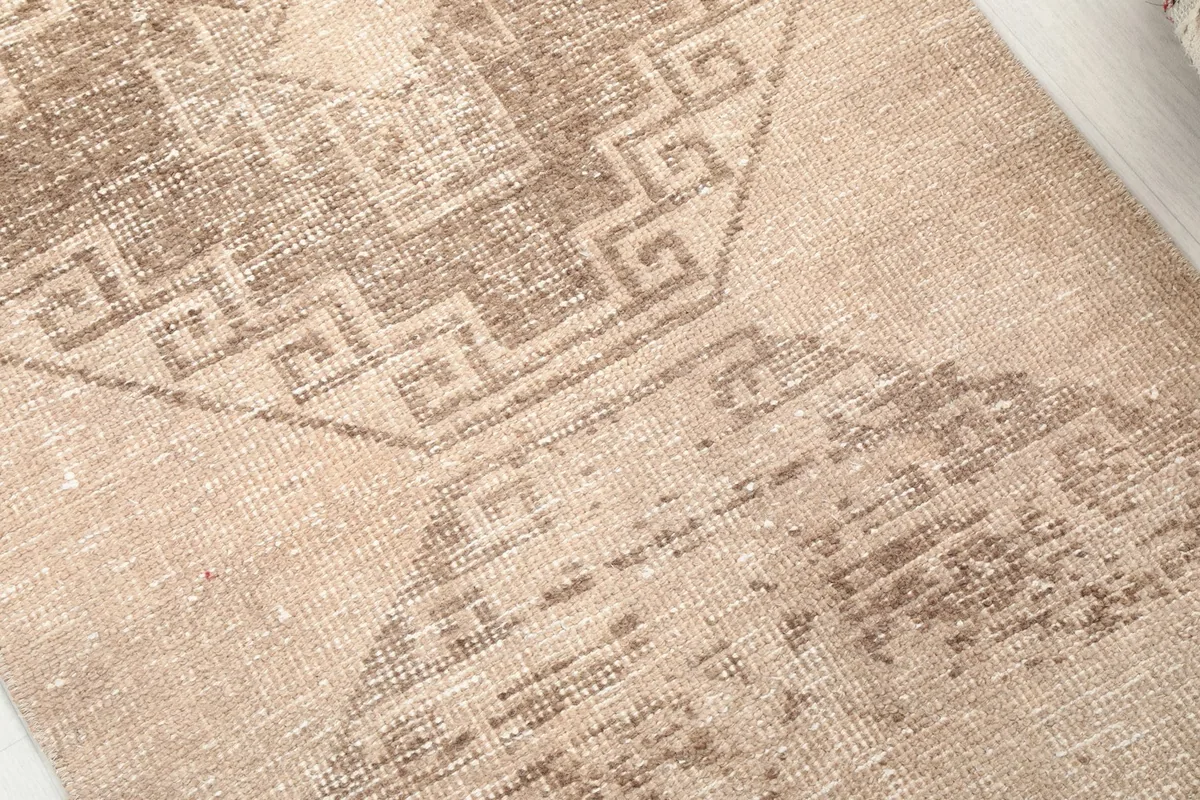 Close-up detail of the hand-knotted wool pile and the distressed brown geometric pattern on the tan field.