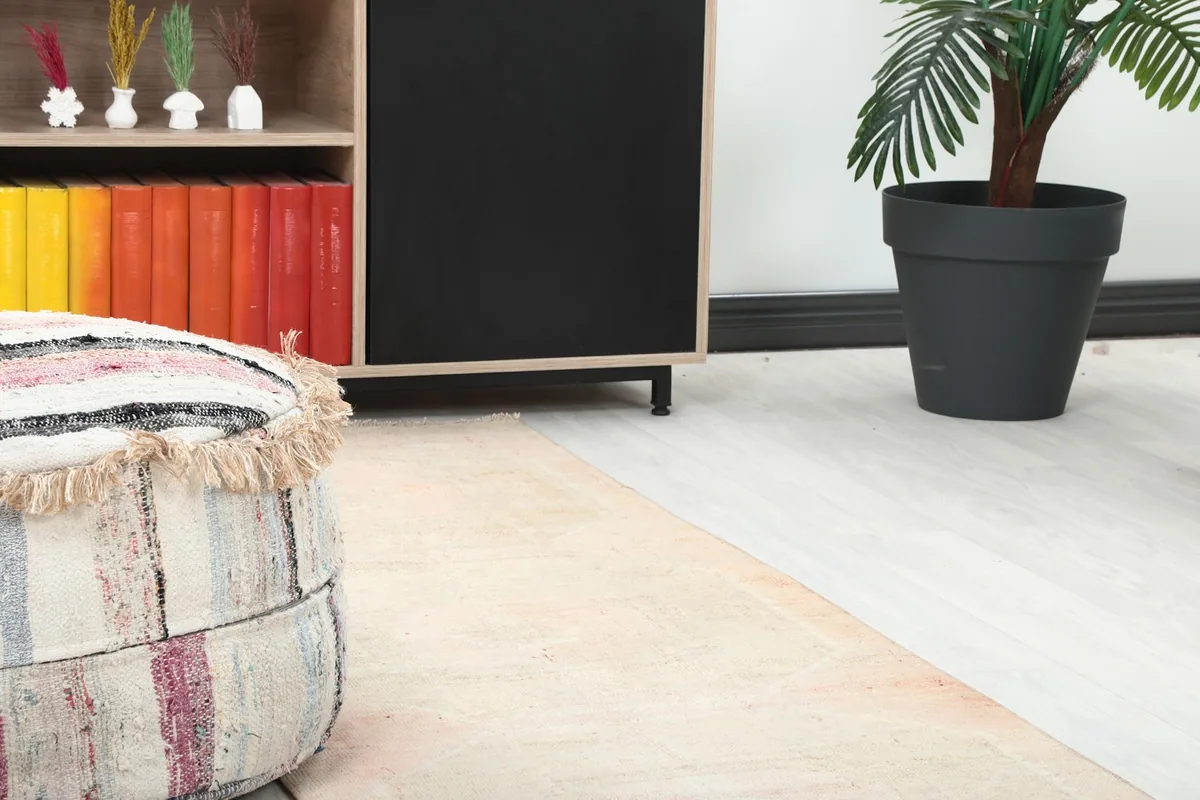 Detail view of the runner rug on the floor next to a colorful ottoman and dark cabinet
