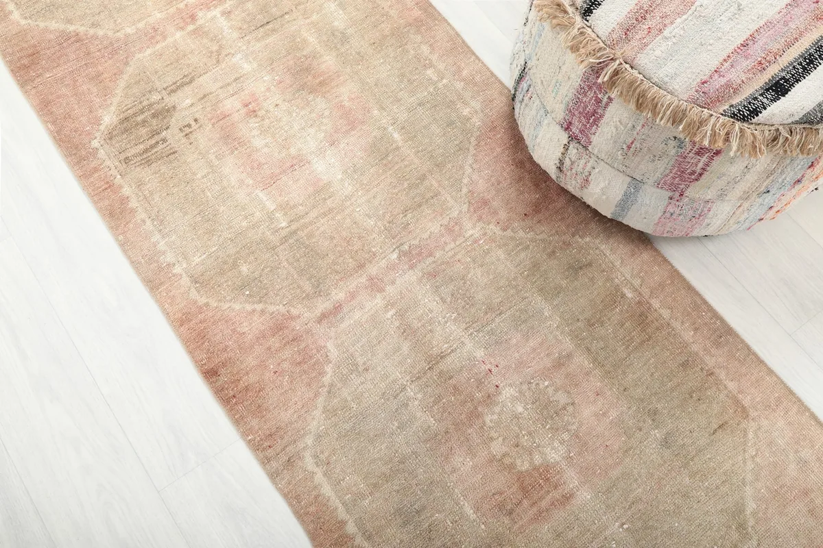 Angled close-up of the runner rug's geometric pattern and beige and rose colors next to an ottoman