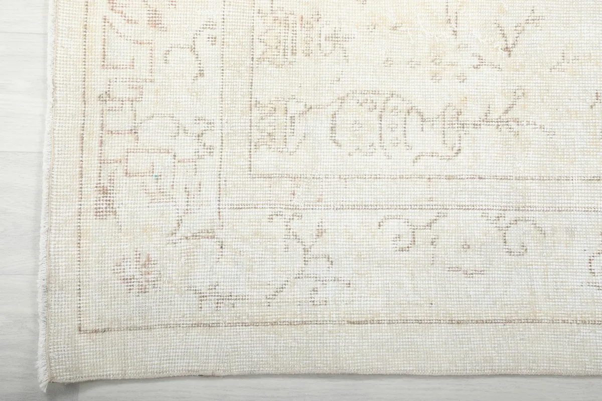 Detail of the rug's border, showing the subtle geometric patterns and soft ivory fringe