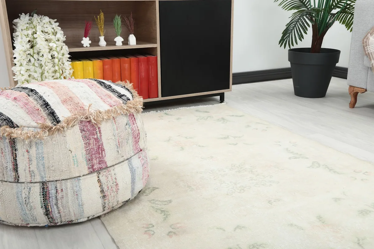 Close-up view of the rug's beige field and subtle rose and green floral patterns next to a pouf