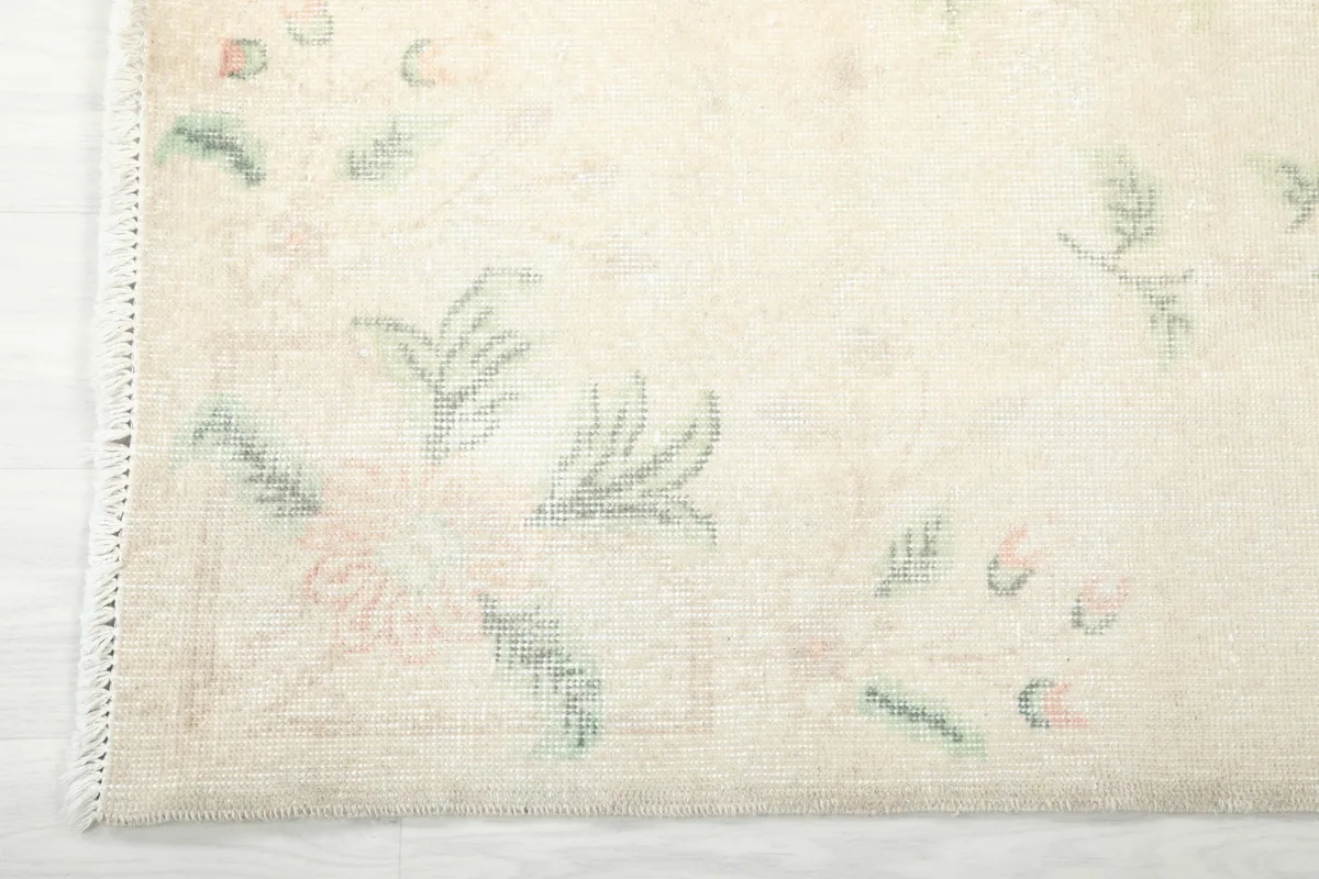 Detail of the rug's edge, showing the subtle fringe and the faded green leaf patterns