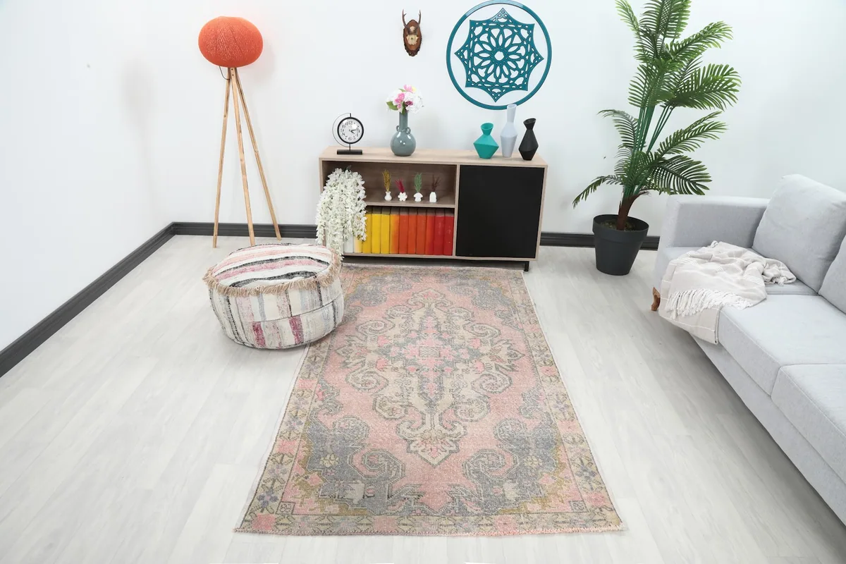 Rose and gray vintage rug placed in a modern living space with a light gray sofa and a pouf.