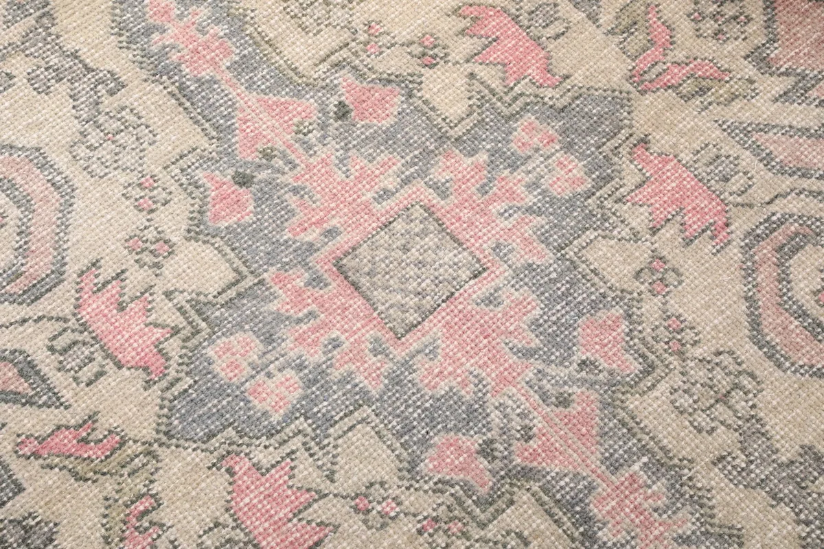 Close-up of the low wool pile, showing the hand-knotted texture and color variations in rose, gray, and beige.
