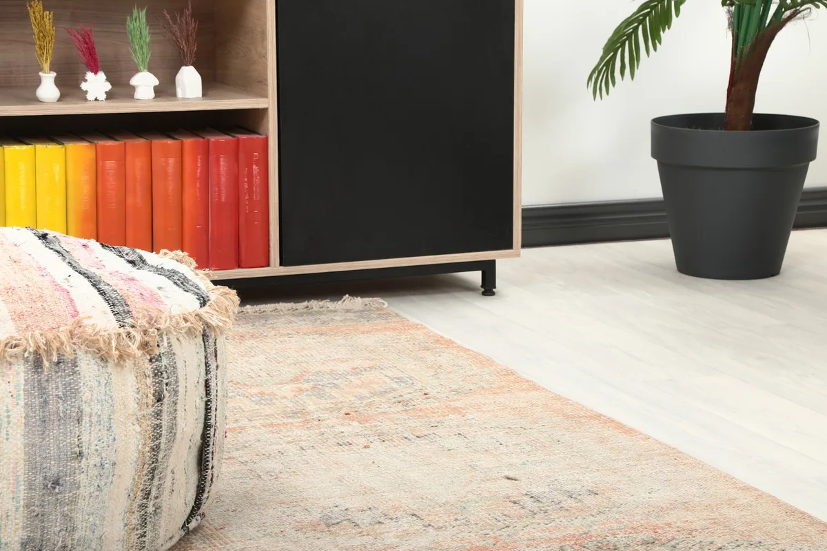 Close-up view of the runner rug's end near a decorative ottoman and bookshelf in a room setting.