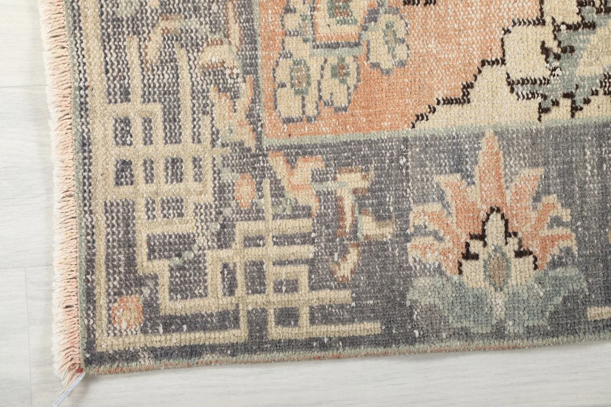 Detailed shot of the rug's corner, showing the gray border with geometric motifs and fringe