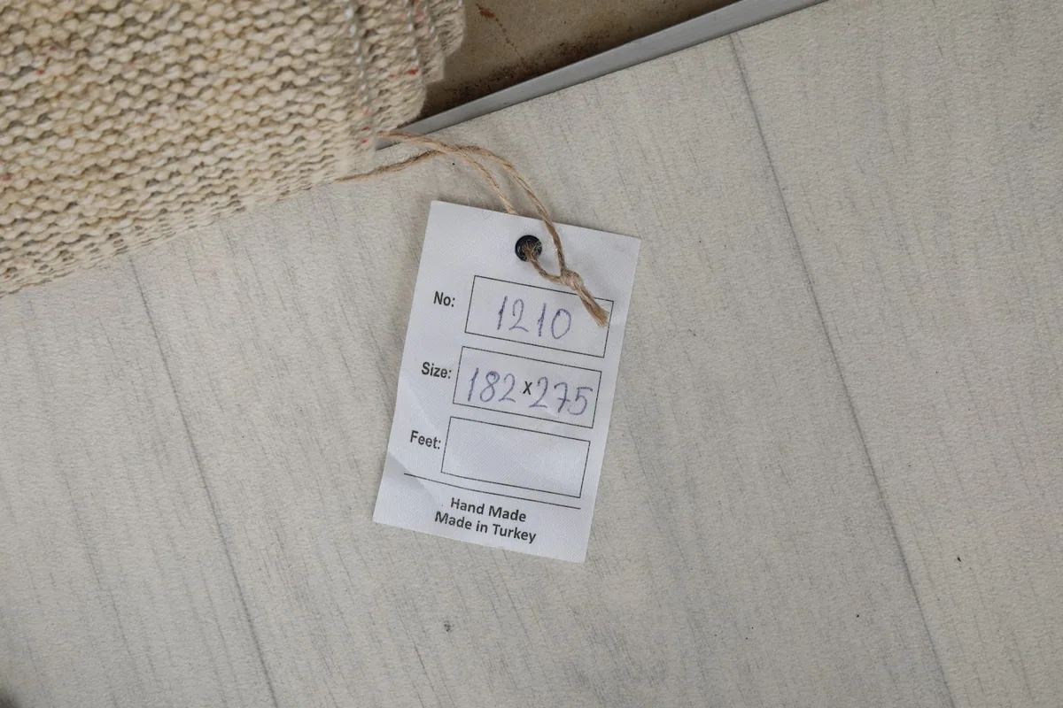 Product tag indicating the rug's dimensions in centimeters (182x275) and its handmade origin