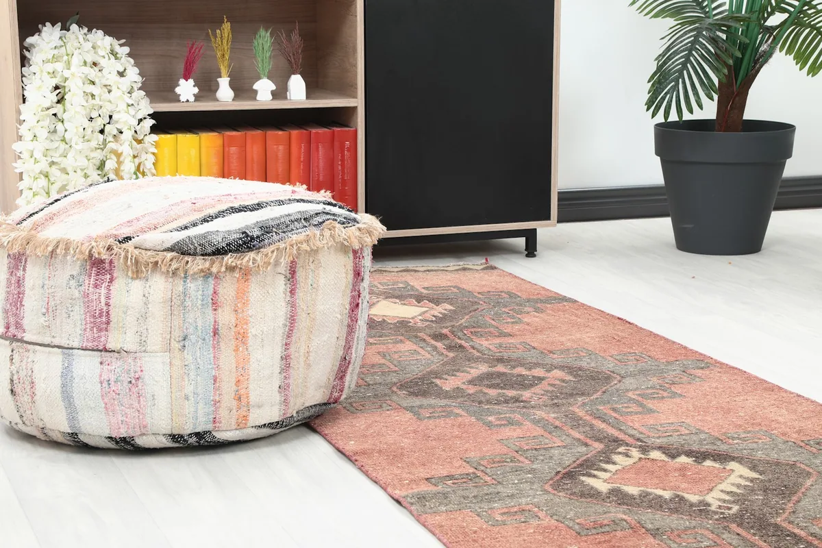 Close-up of the runner rug in a room, showing its texture next to a striped ottoman and bookshelf.