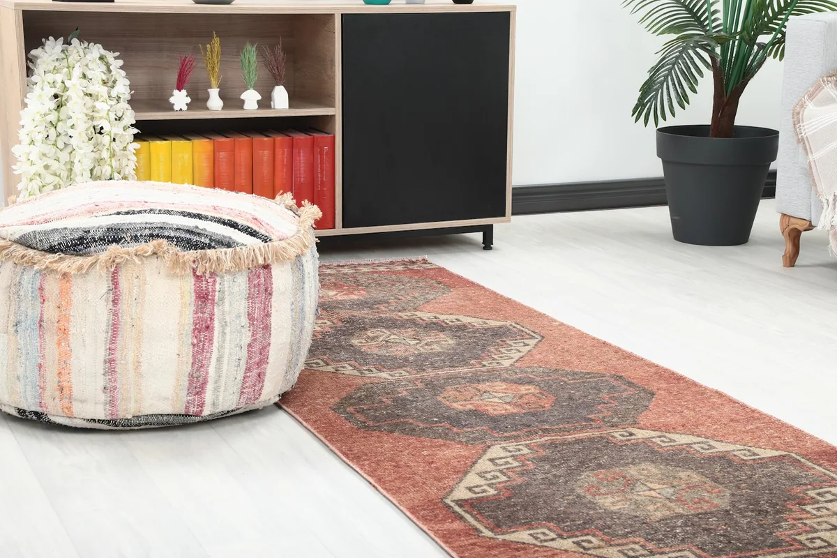 Close-up angled shot of the runner rug next to a decorative pouf and wooden cabinet in a home setting.