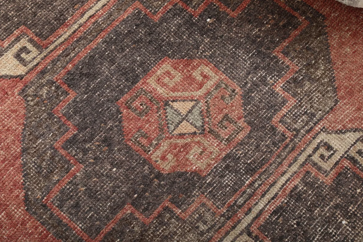 Extreme close-up of a tribal medallion, revealing the intricate knotting and color blend of rust, charcoal, and beige.