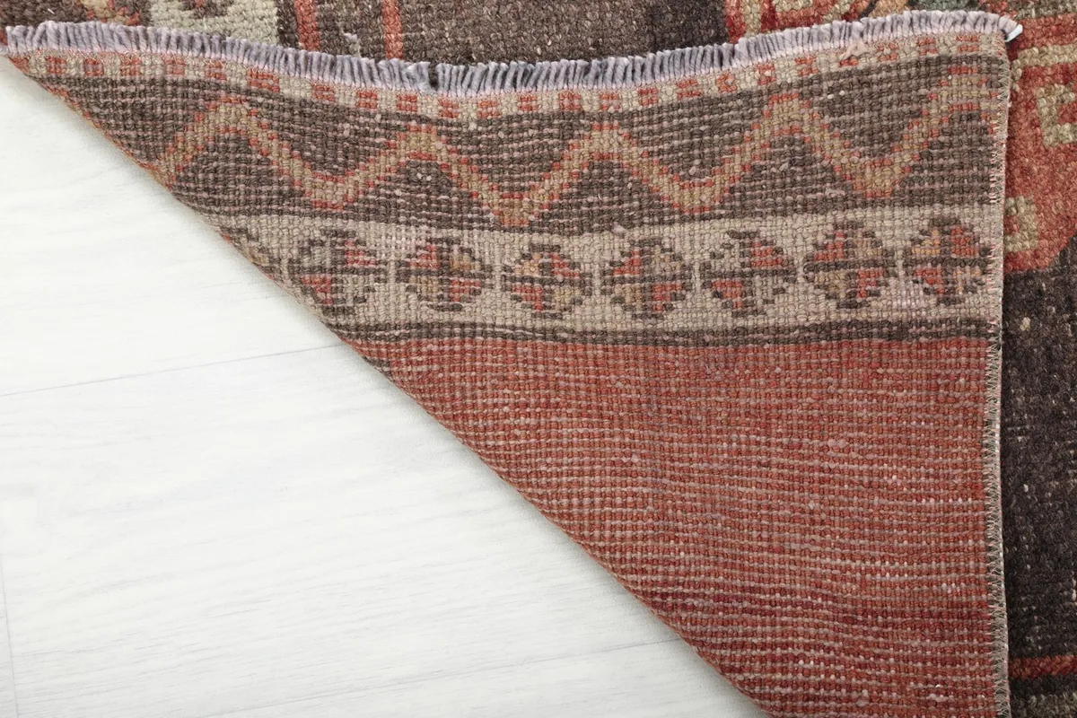 Underside of the rug revealed by a folded corner, showing the hand-knotted cotton foundation and wool pile.