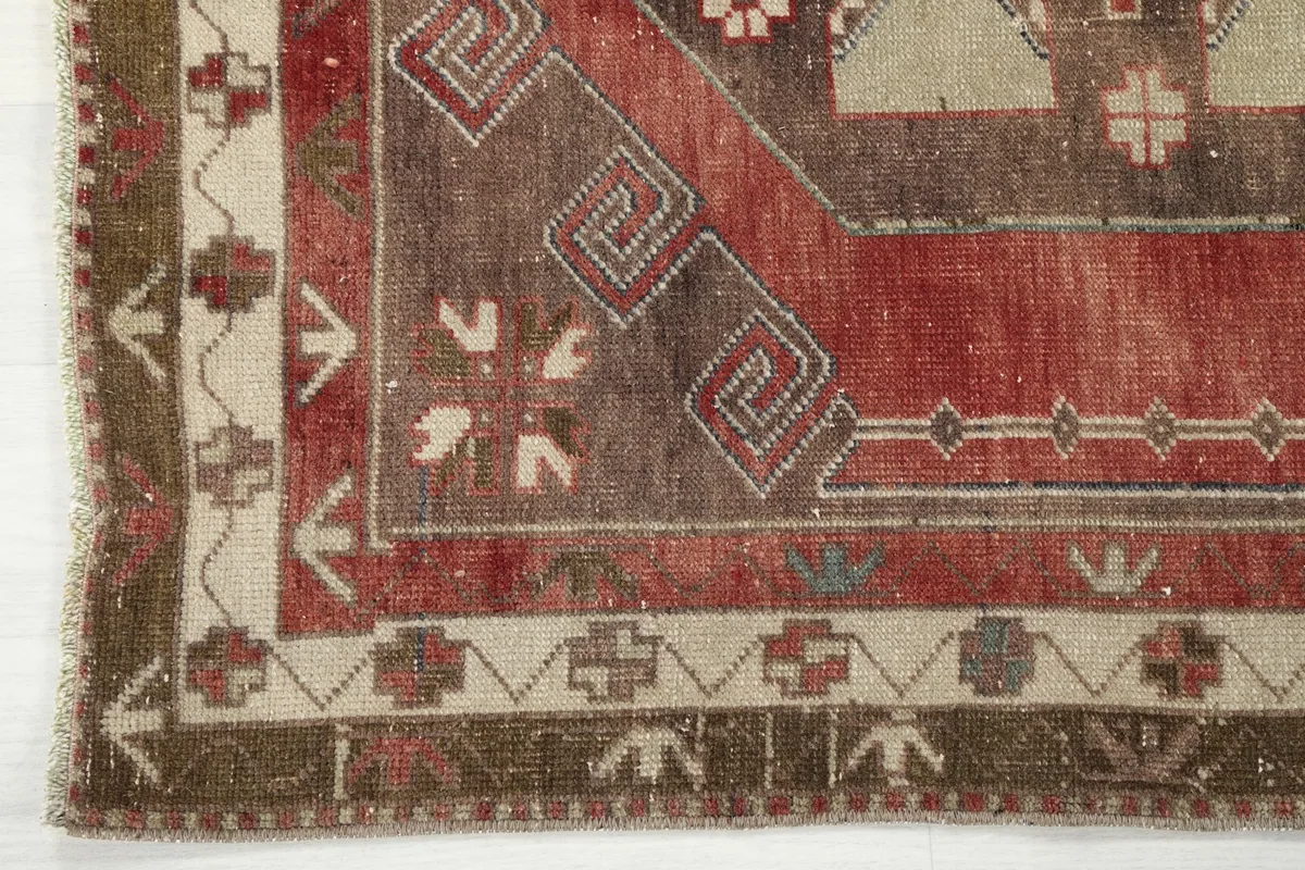 Detailed view of the rug's border design, featuring beige and olive patterns alongside the main red field