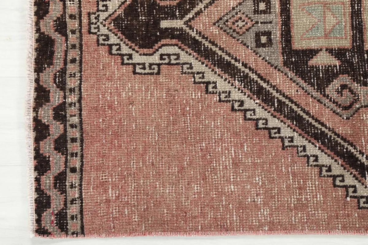 Close-up of the border and edge of the rose runner rug, showing the faded wool texture